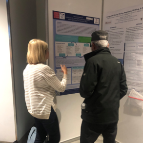 female, Liz, standing next man looking at the poster