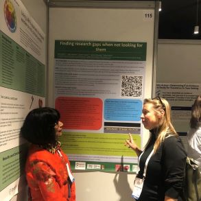 female, mala, standing next to another female looking at the poster 