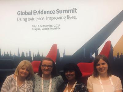 Cardiff Evidence Synthesis Team, 4 ladies, standing in front of the conference sign 